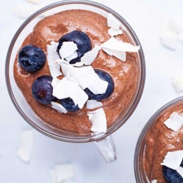 Two mini cups with blended chocolate chia mousse and topped with blackberries and coconut shreds.