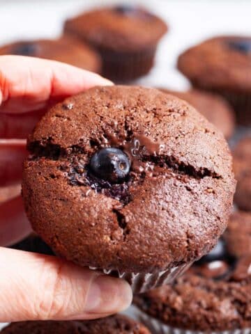 A hand holding a chocolate berry muffin.