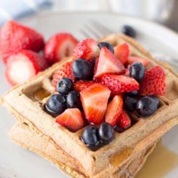 Three waffles stacked on top of each other and topped with maple syrup and fresh berries.