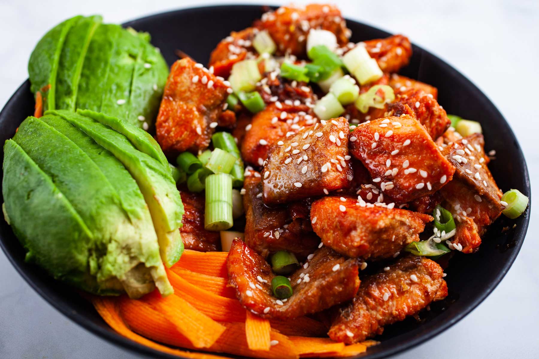 Cooked salmon poke bowl with avocado, carrots, and onions.