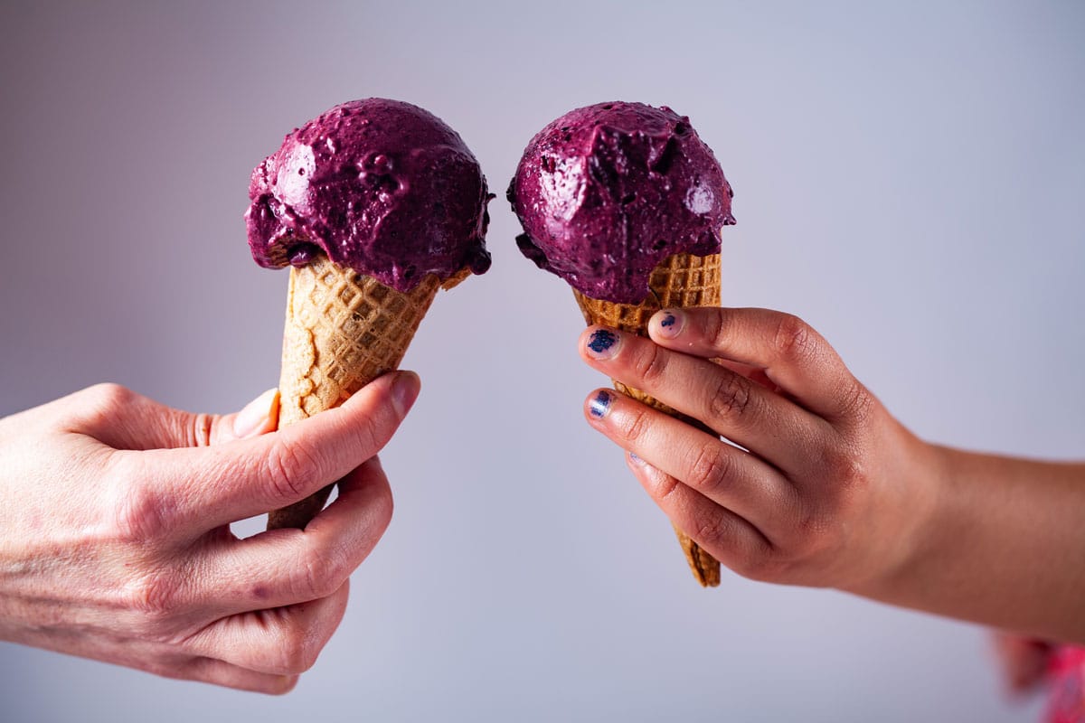 Two hands carrying each a berry ice cream on a cone.