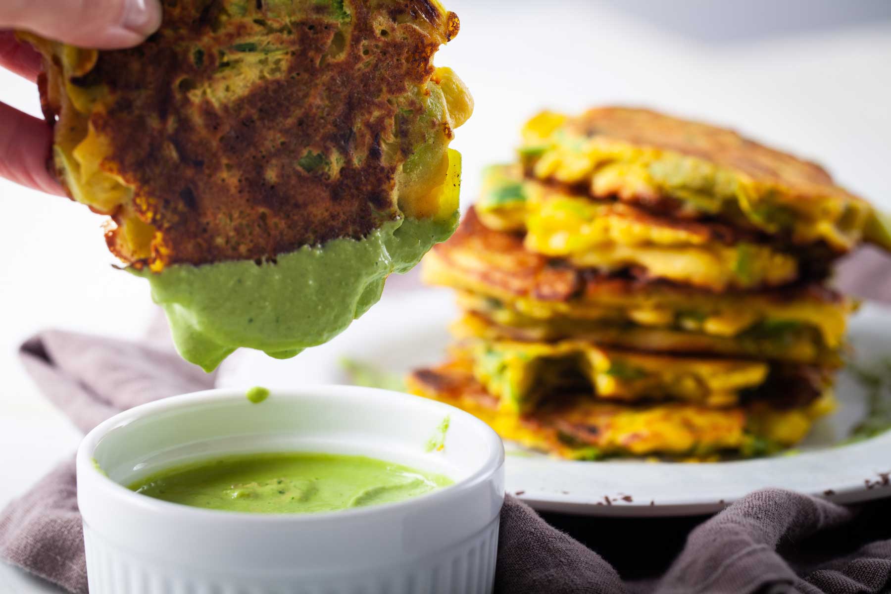 A hand dipping a leek fritter into a green sauce.