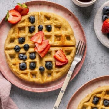 A round waffle on a plate topped with fresh fruit.