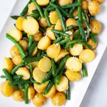 Olive oil coated mini potatoes and green beans on a serving plate.