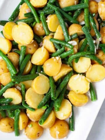 Olive oil coated mini potatoes and green beans on a serving plate.