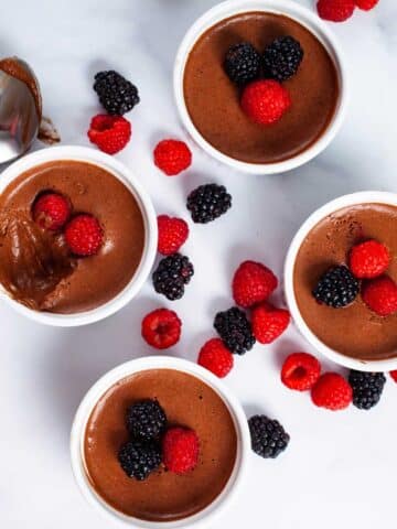 Four ramekins filled with chocolate mousse and topped with fresh berries.