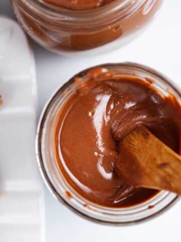 A wooden knife resting in silky, creamy chocolate peanut butter in a jar.