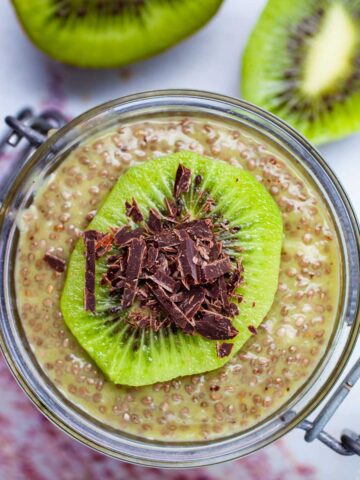 A cup filled with kiwi chia pudding topped with a slice of fresh kiwi fruit and shaved chocolate.