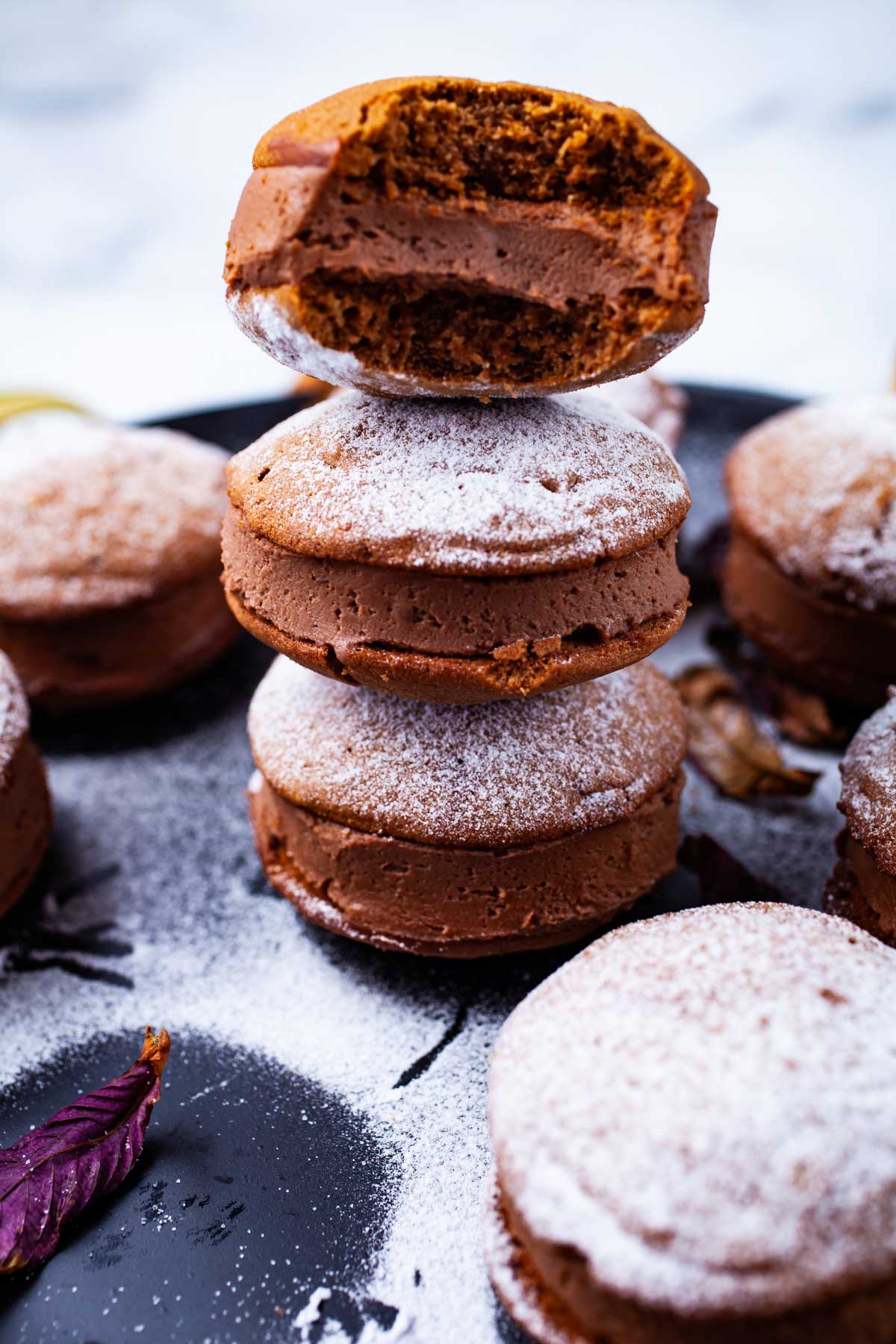 Sandwich cookies filled with a chocolate mascarpone frosting stacked on top of each other and dusted with powder sugar.