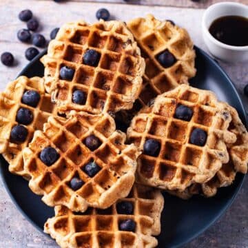 Oat flour waffles on a plate topped with blueberries.