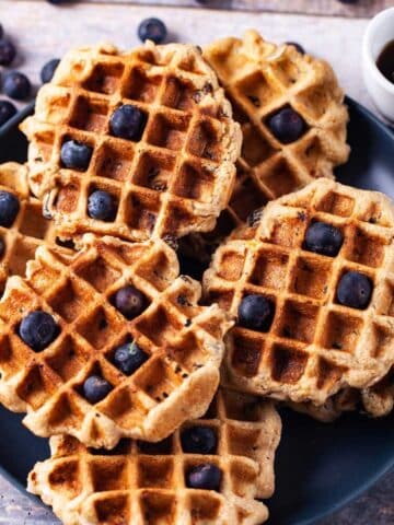 Oat flour waffles on a plate topped with blueberries.