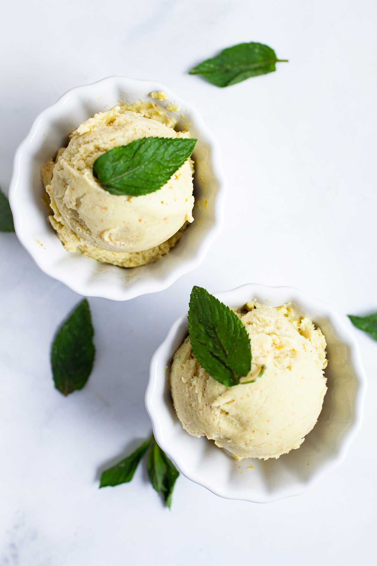 Two small bowls with pineapple avocado ice cream and topped with fresh mint leaves.