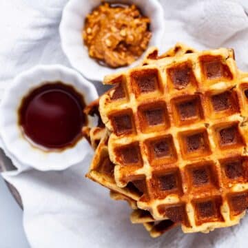 Plantain waffles next to a small bowl with maple syrup and a small bowl with nut butter.