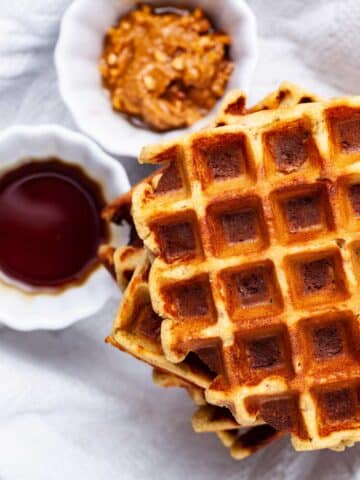 Plantain waffles next to a small bowl with maple syrup and a small bowl with nut butter.