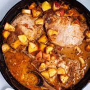 Cast iron skillet pork chops with apples, squash and pan juices served on a table.