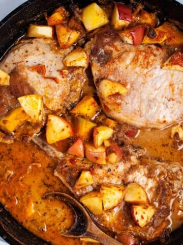 Cast iron skillet pork chops with apples, squash and pan juices served on a table.