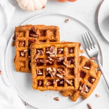 Waffles on a plate topped with syrup and pecans.