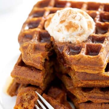 Three waffles stacked on top of each other and topped with syrup and a dollop of cream.