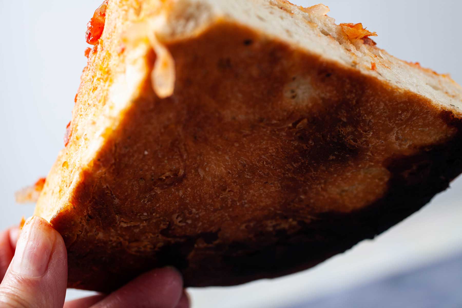 A hand holding a slice of pizza up so you can see the bottom of the crust.