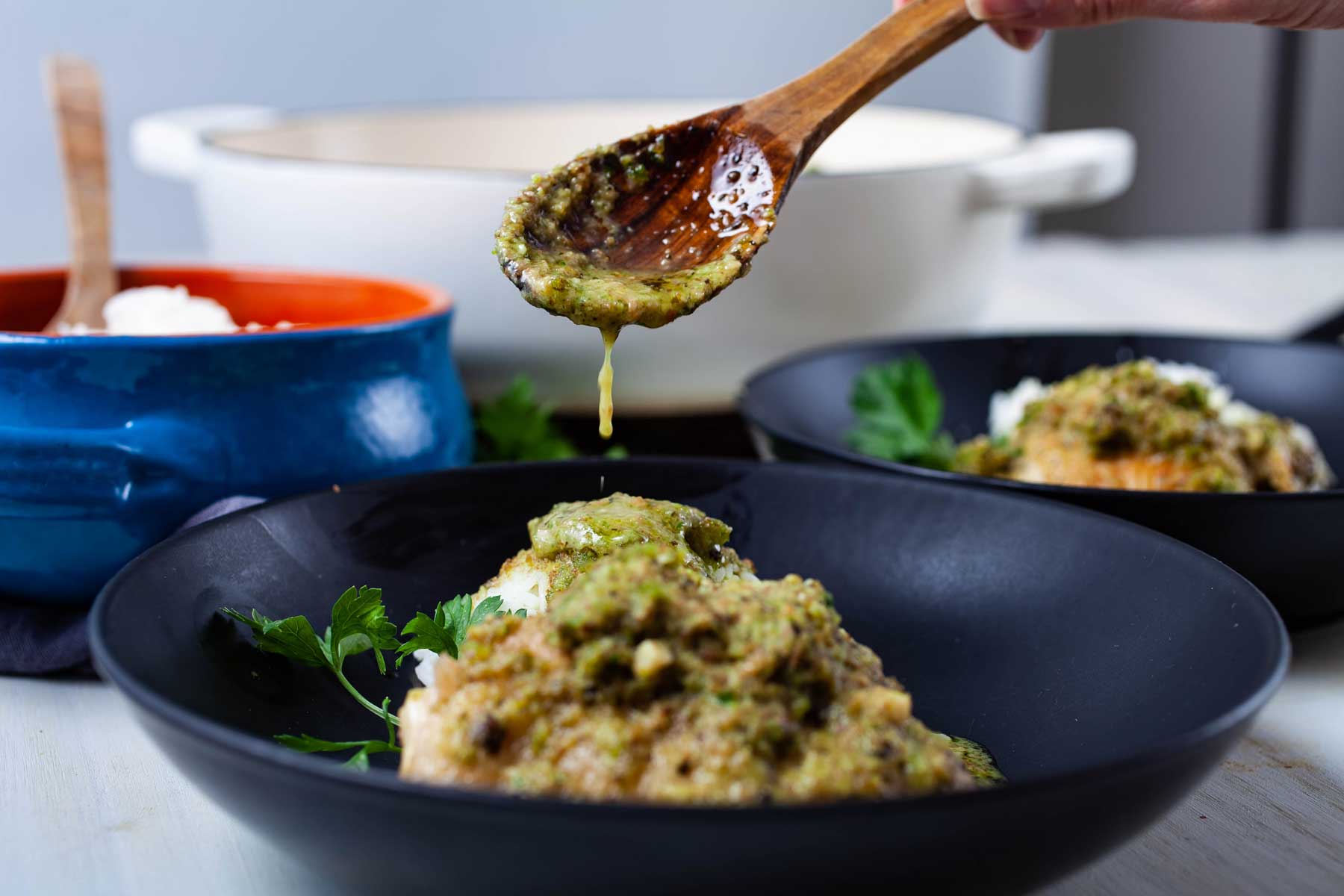 A spoon serving pesto sauce on top of pan-seared chicken thigh.