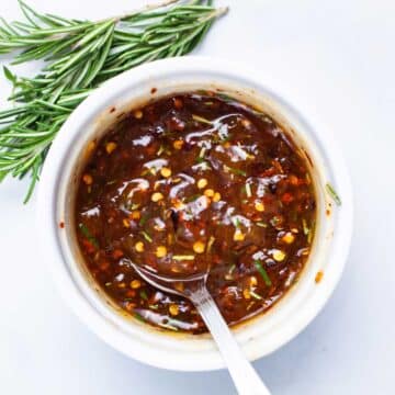 A spoon resting in a ramekin filled with spiced apricot jam.