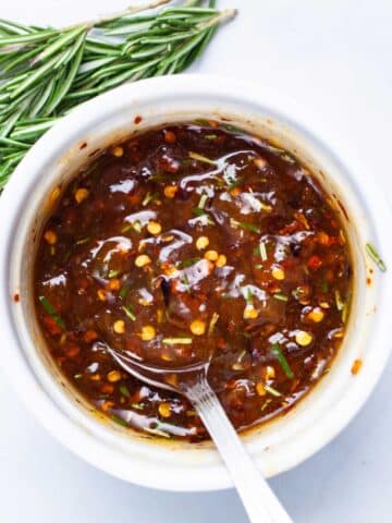 A spoon resting in a ramekin filled with spiced apricot jam.