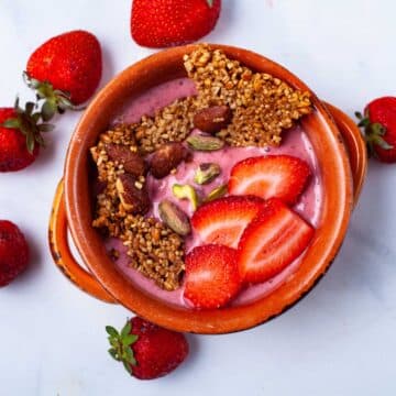 A strawberry smoothie bowl topped with toasted oats, nuts, and fresh strawberries.