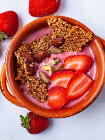 A strawberry smoothie bowl topped with toasted oats, nuts, and fresh strawberries.