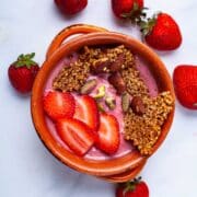 A strawberry smoothie bowl topped with toasted oats, nuts, and fresh strawberries.