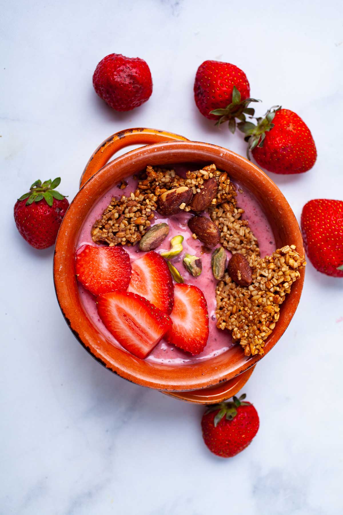 A strawberry smoothie bowl topped with toasted oats, nuts, and fresh strawberries.