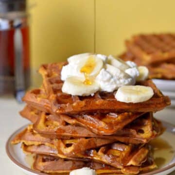 A stack of waffles topped with syrup, banana slices, and whip cream.