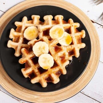 Three waffles on a plate topped with syrup and banana slices.