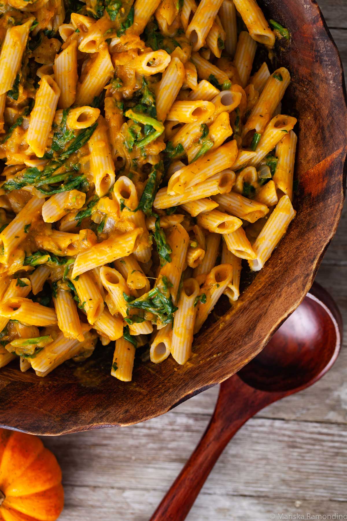 A large wooden bowl filled with creamy pumpkin penne pasta and spinach.