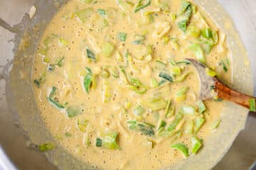 A wooden spoon resting in a batter with cooked leek.