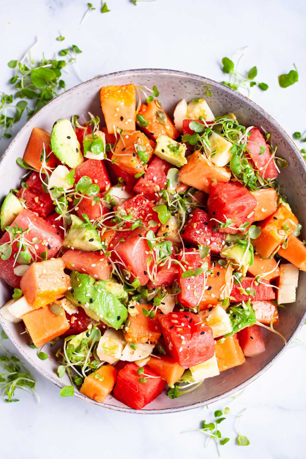 A watermelon fruit salad with papaya and avocado and crunchy seeds served in a bowl.