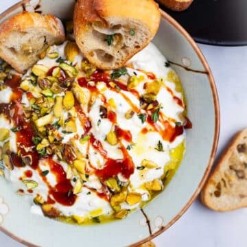 Whipped ricotta with honey in a bowl, topped with pistachios and served with crostini.