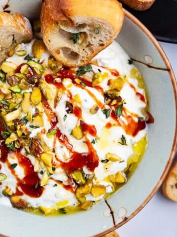 Whipped ricotta with honey in a bowl, topped with pistachios and served with crostini.