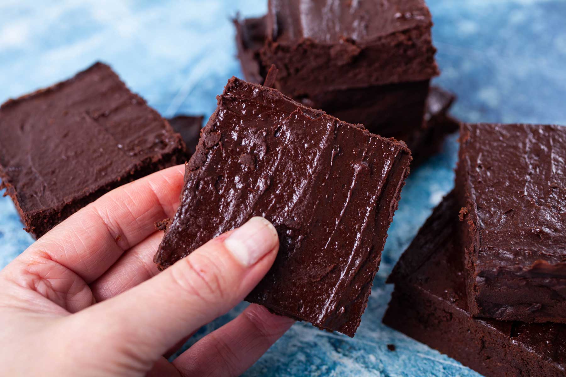 A hand holding up a square date brownie with a shiny crust.