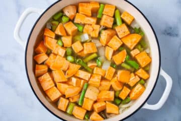 Chopped sweet potatoes, asparagus, onions, and broth in a large Dutch pan.
