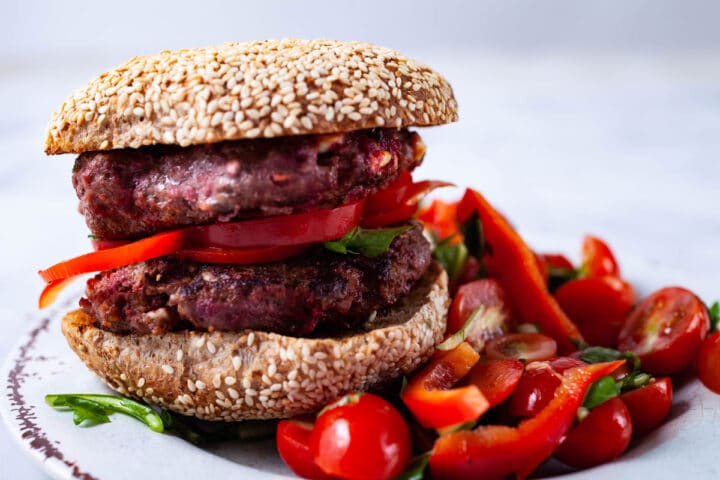 A double hamburger in a bun with a seasoned healthy salad on the side.