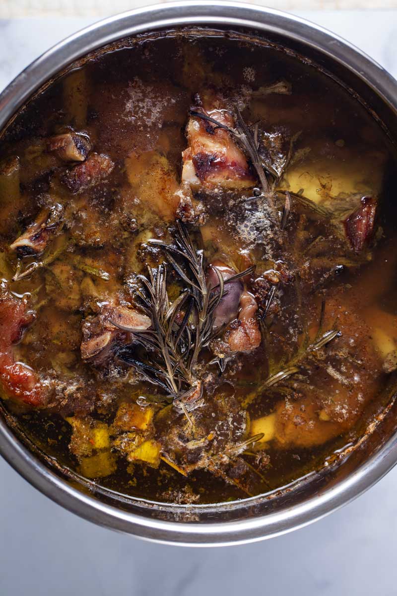 A pot filled with cooked bone broth and meat bones.