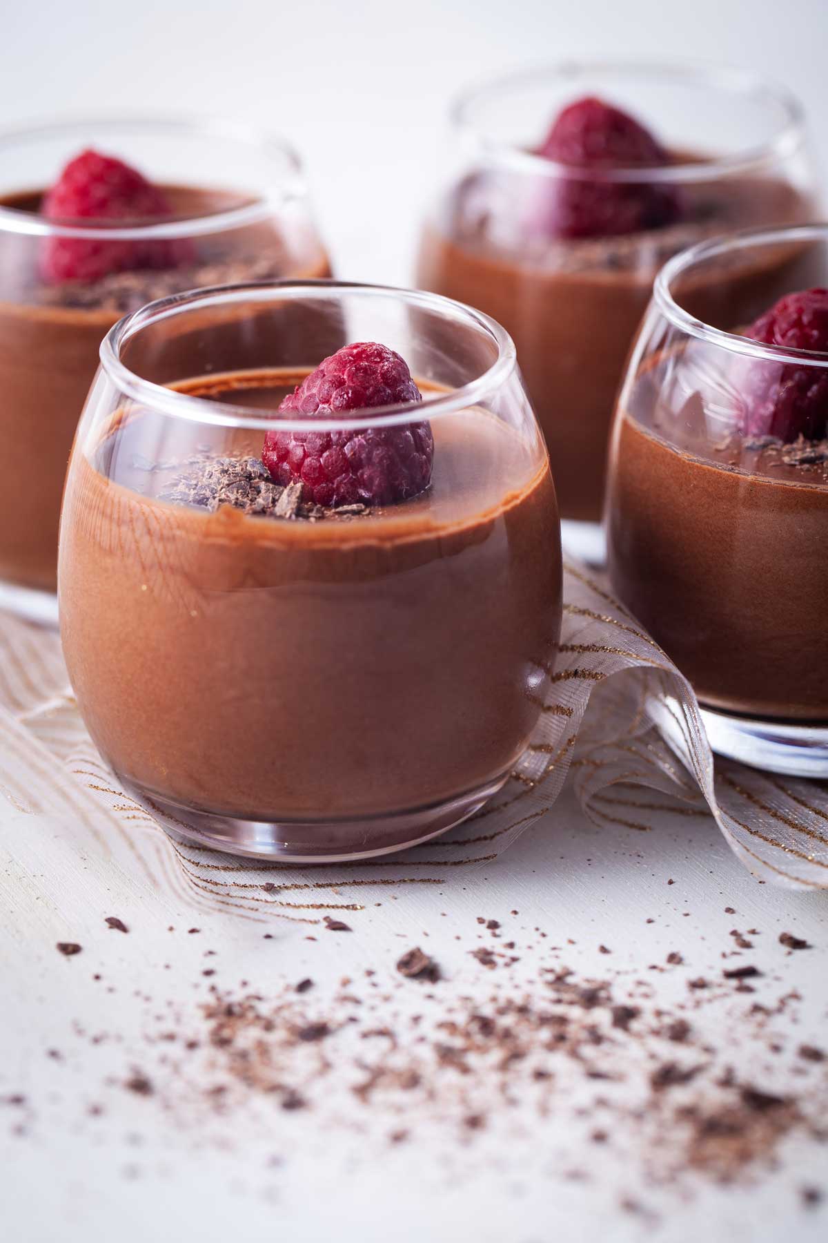 Chocolate coffee mousse in small cups topped with shaved chocolate and a raspberry.