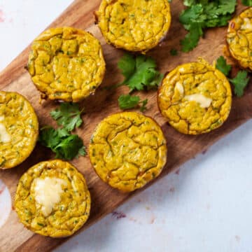 Cheesy egg muffins assorted on a wooden board with fresh parsley leaves.