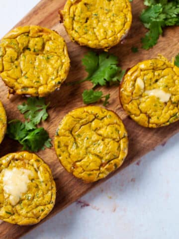 Cheesy egg muffins assorted on a wooden board with fresh parsley leaves.