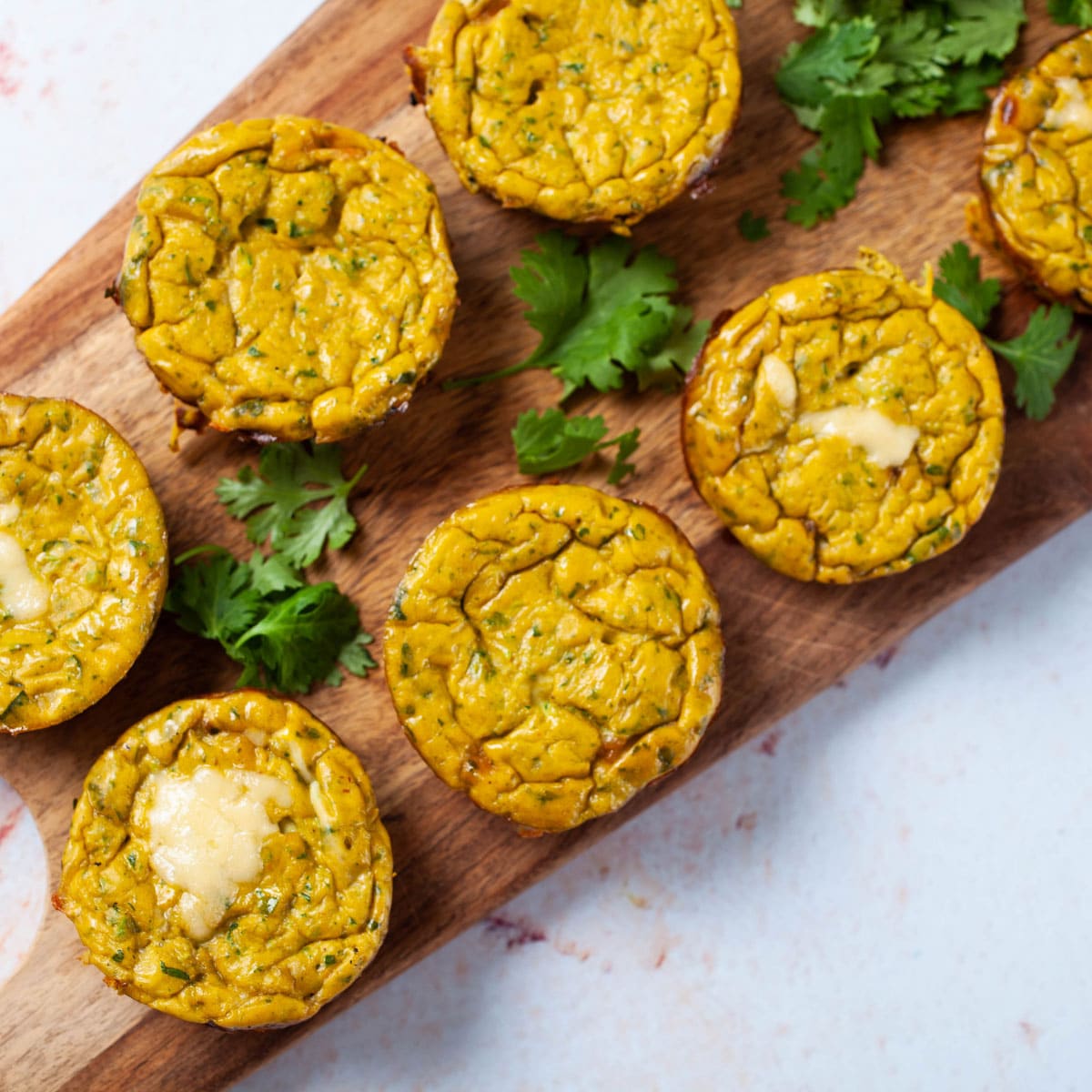 Cheesy egg muffins assorted on a wooden board with fresh parsley leaves.