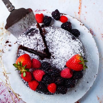 A mini low carb chocolate cake served with fresh berries and topped with powdered sugar.