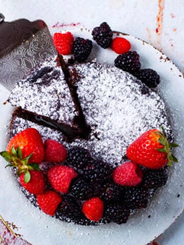 A mini low carb chocolate cake served with fresh berries and topped with powdered sugar.