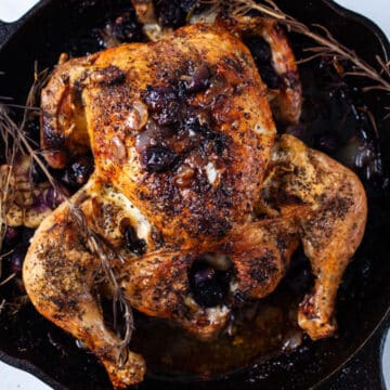 One whole roasted browned chicken in a cast-iron pan with pan juices.