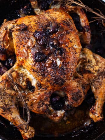 One whole roasted browned chicken in a cast-iron pan with pan juices.