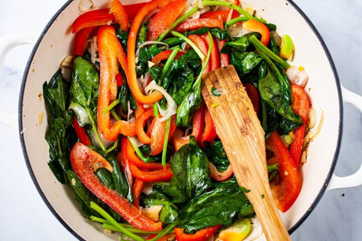 Sauteed veggies like red bell pepper, spinach leaves, and onions in a pan.